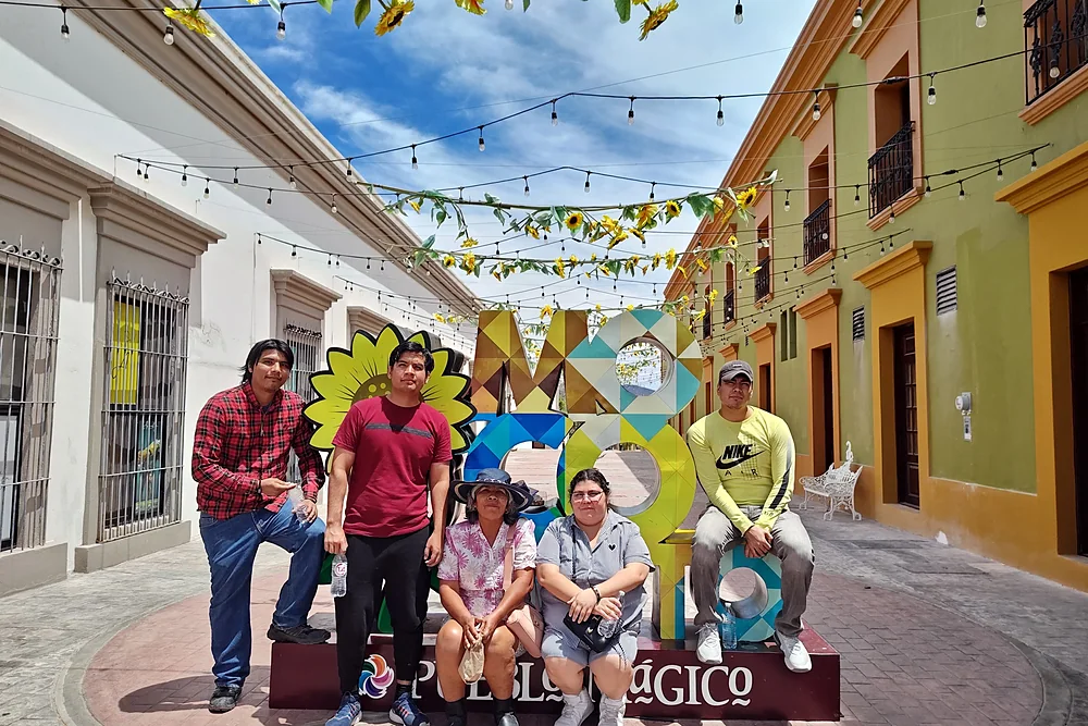 Viajeros sentados en las letras de Mocorito, Pueblo Mágico